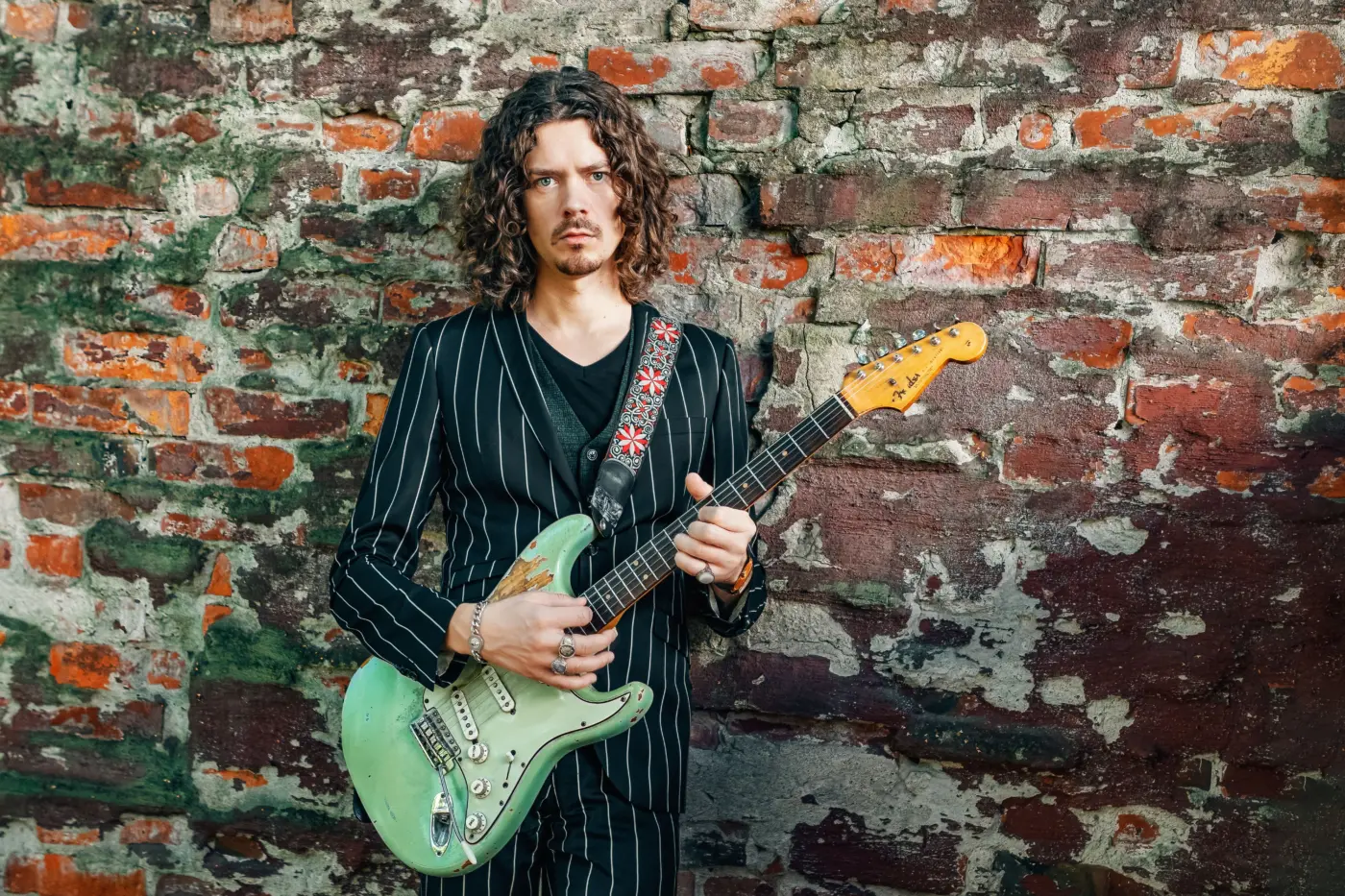 Mies seisoo pidellen vihreää Fender Stratocaster -tyylistä kitaraa.